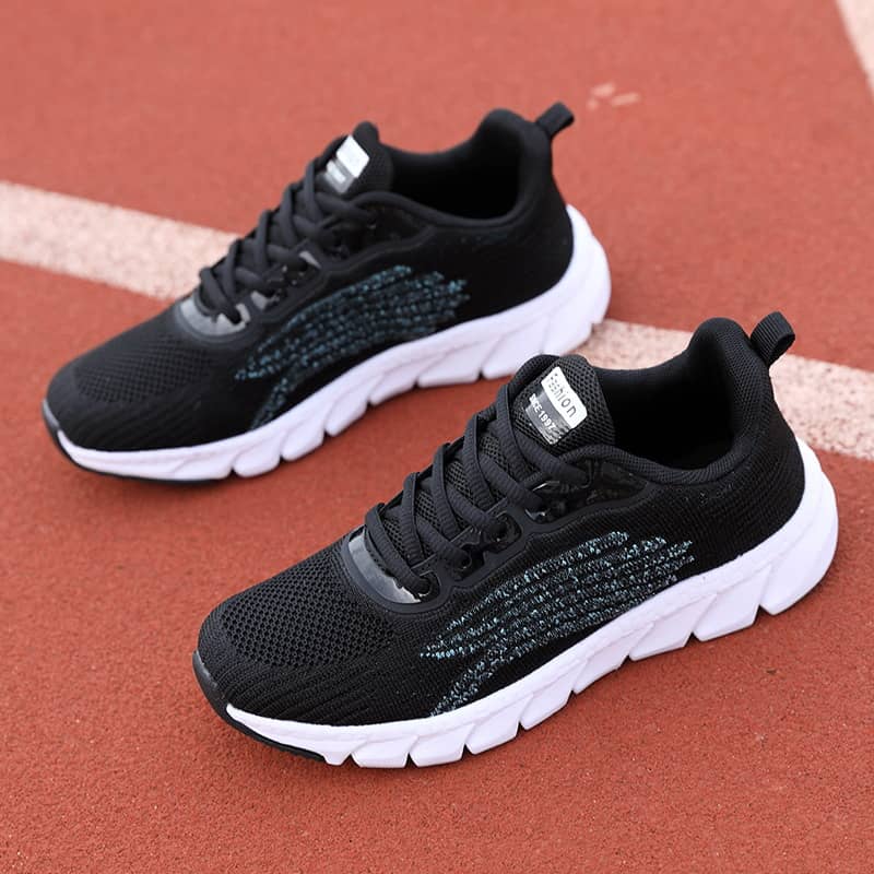 Black athletic running shoes with white soles on a red track surface