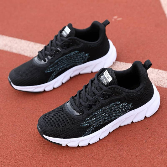 Black athletic running shoes with white soles on a red track surface