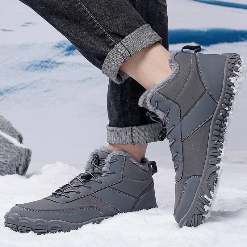 Gray winter hiking boots with fur lining and rugged soles on snowy ground