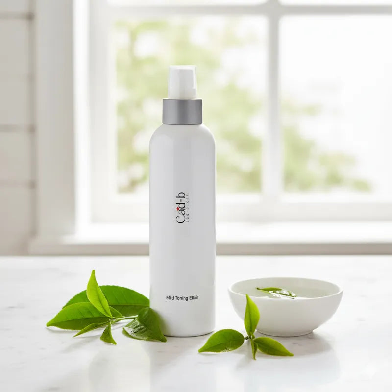 White bottle with silver cap on a white surface with green leaves and a bowl in the background.