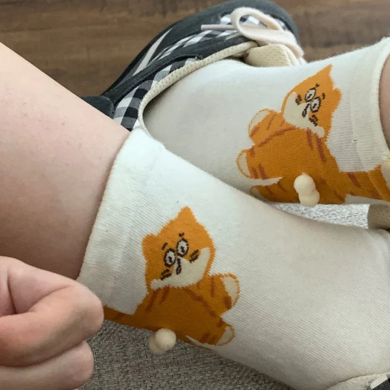 White socks with cute orange cartoon cat design and small pom pom, worn with sneakers