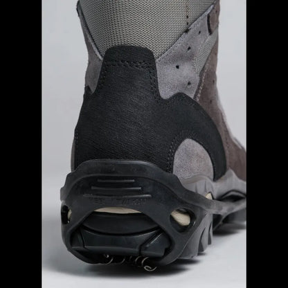 Close-up rear view of a gray and black outdoor boot with a rugged black sole and metal crampons attached, photographed on a light gray studio background.