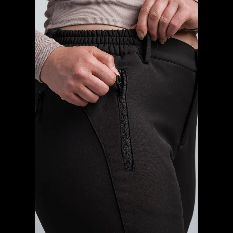 Close-up of a person wearing black pants, showing the elastic waistband, zippered side pocket, and hands adjusting the waistband.