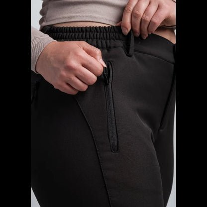 Close-up of a person wearing black pants, showing the elastic waistband, zippered side pocket, and hands adjusting the waistband.