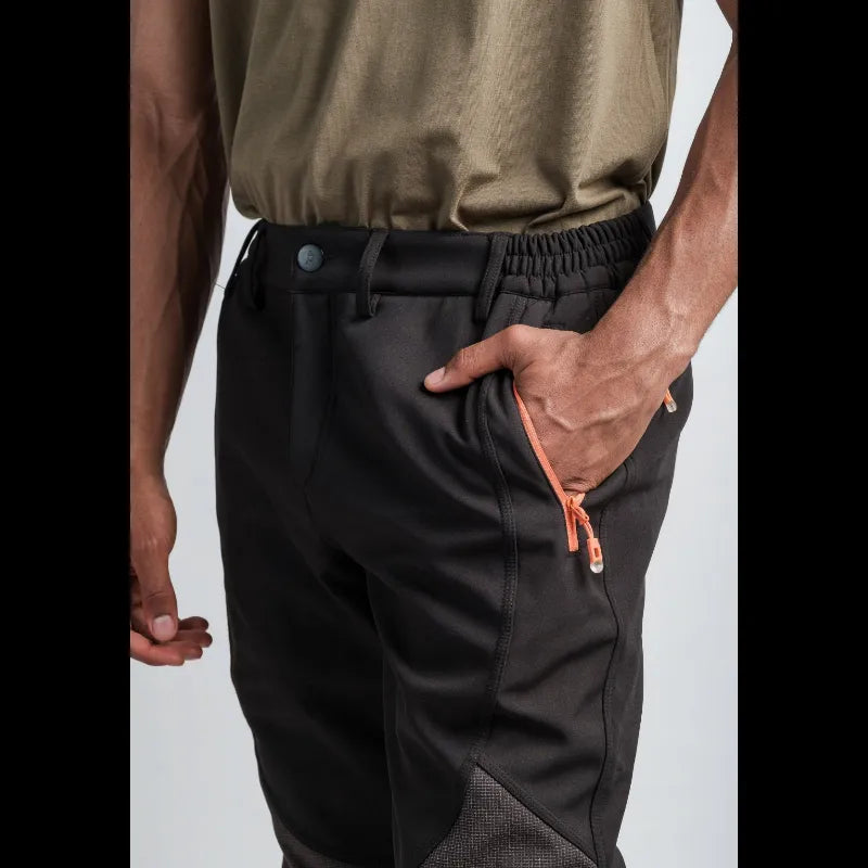 Close-up of a person wearing black athletic pants with an orange drawstring and side pocket, paired with an olive green shirt, against a light gray background.