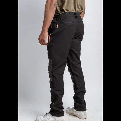 A person shown from the back wearing black technical pants with orange zipper accents, paired with a khaki shirt and white sneakers, against a light gray studio background.