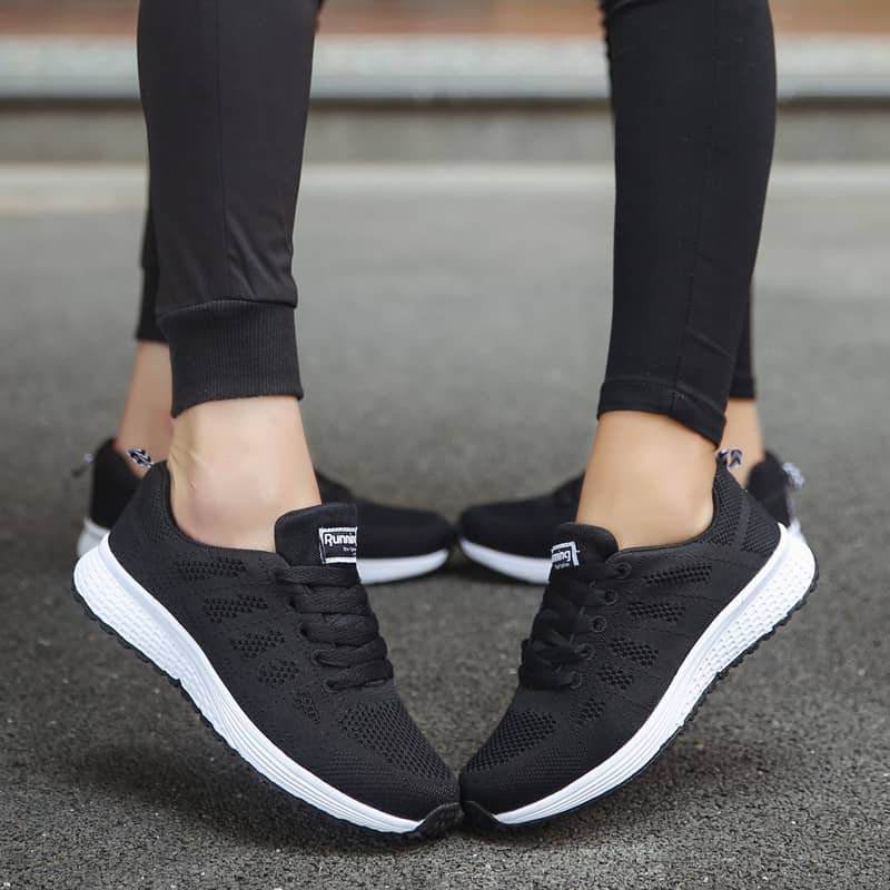 Black running shoes with white soles worn by a person on a blurred background