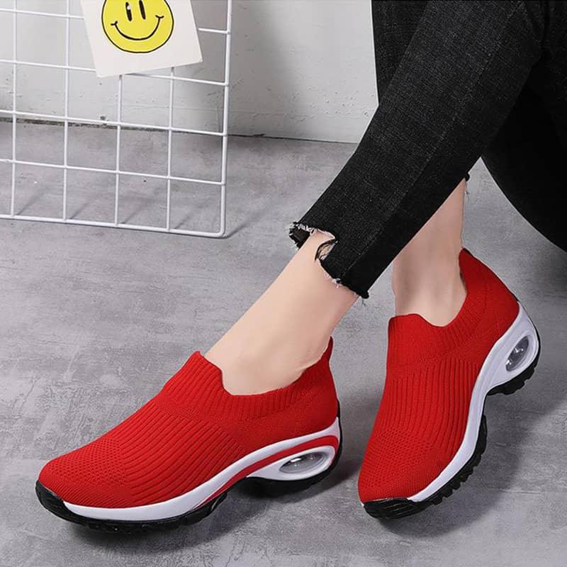 Red slip-on shoes with white soles worn by a person on a gray floor.