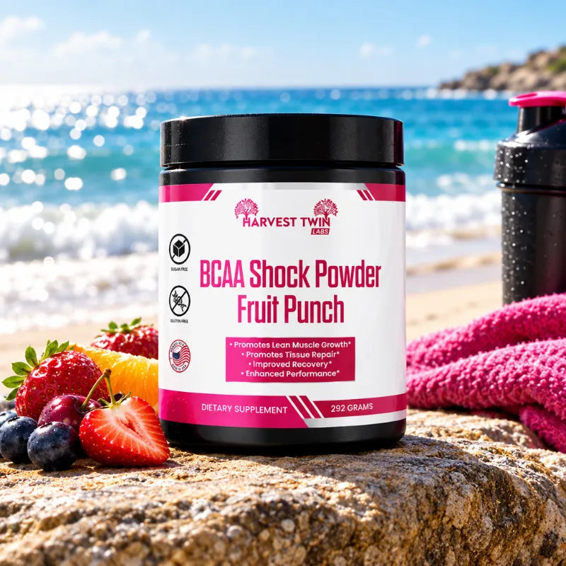 A tub of Harvest Twin Aged BCAA Shock Powder Fruit Punch supplement placed on a beach scene, surrounded by fresh strawberries, blueberries, and an orange, with a pink towel and a shaker bottle in the background.