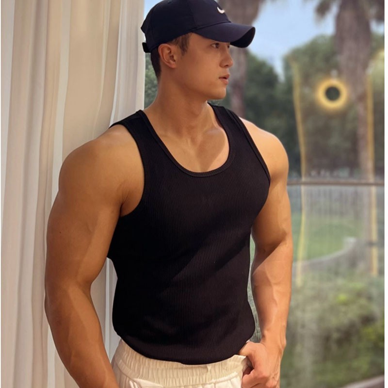 Man wearing a black tank top and cap leaning against a curtain outdoors.