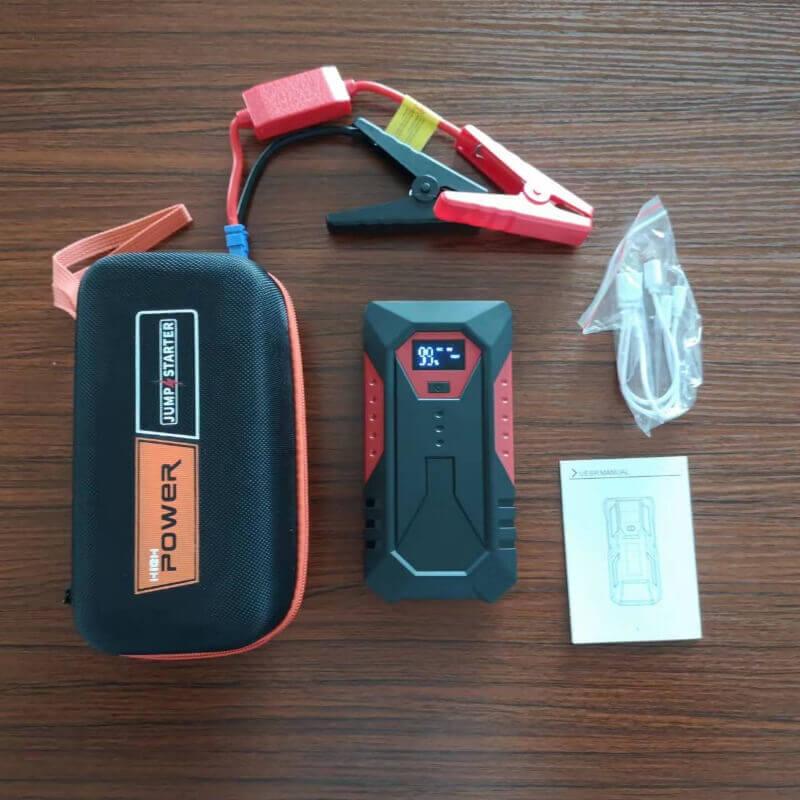 Portable car jump starter kit with battery pack, clamps, USB cable, case, and manual on wood surface