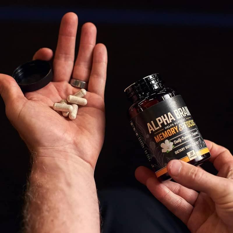 Person holding Alpha Brain memory and focus supplement bottle and capsules