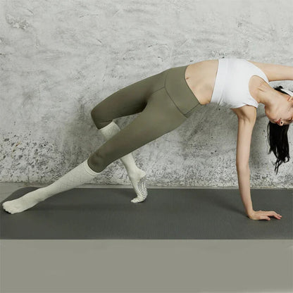 Woman doing yoga in activewear and non-slip socks on an exercise mat indoors