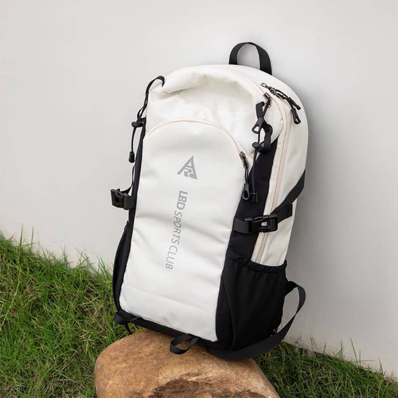 White and black backpack on a rock with grass and a white wall background