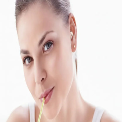 A close-up portrait of a woman with her hair pulled back, wearing small gold stud earrings and holding a yellow straw against her lips, set against a bright white background.