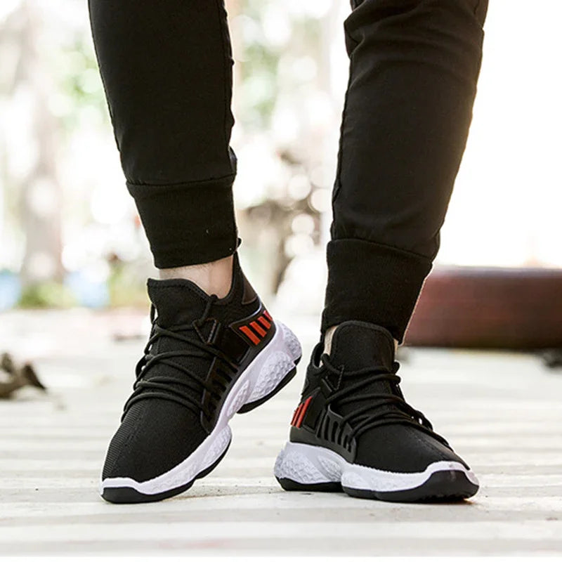 Close-up of person wearing black and white athletic sneakers with red accents and black joggers on outdoor path