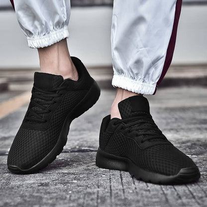 Black athletic shoes worn with light gray pants on a textured surface
