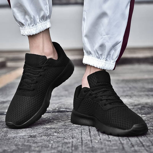 Black athletic shoes worn with light gray pants on a textured surface