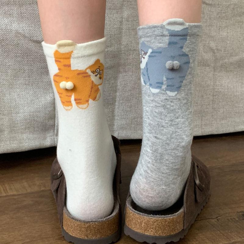 Person wearing mismatched cat socks with cartoon cat designs and textured tails