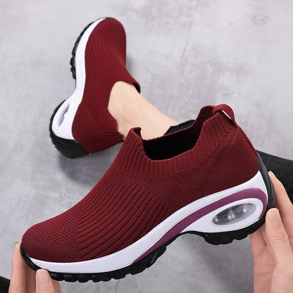 Maroon slip-on sneakers with white sole held by a hand on a gray background