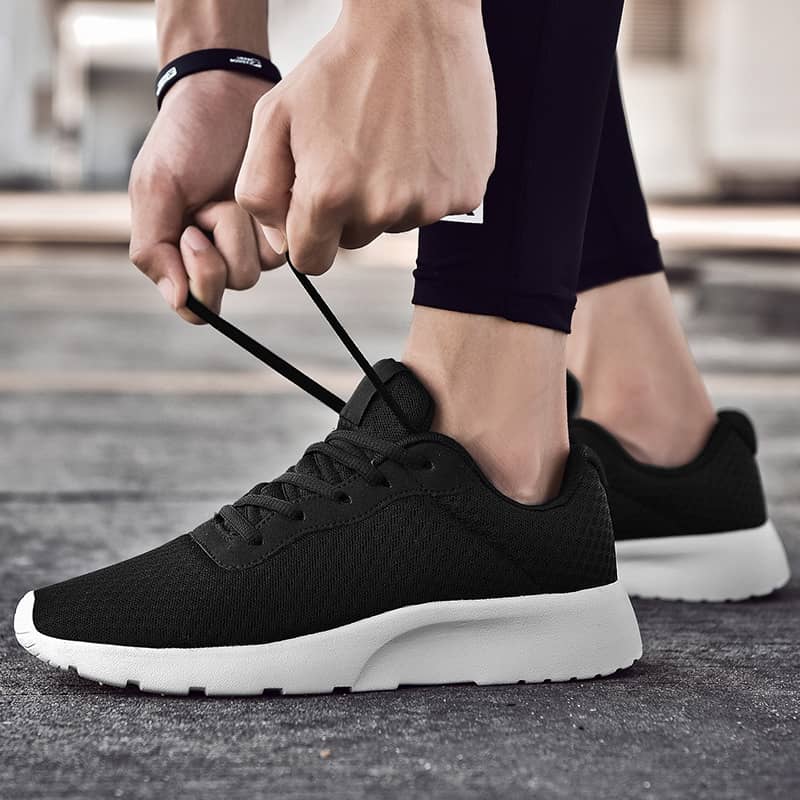 Person tying black running shoes with white soles on a blurred outdoor background