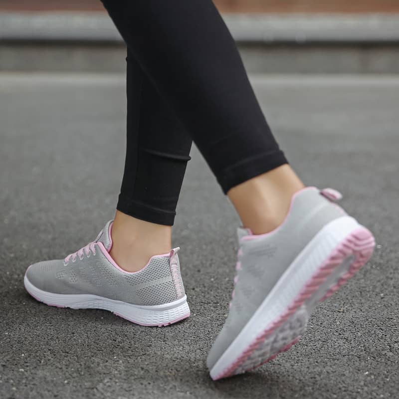 Gray sneakers with pink soles worn on a concrete surface